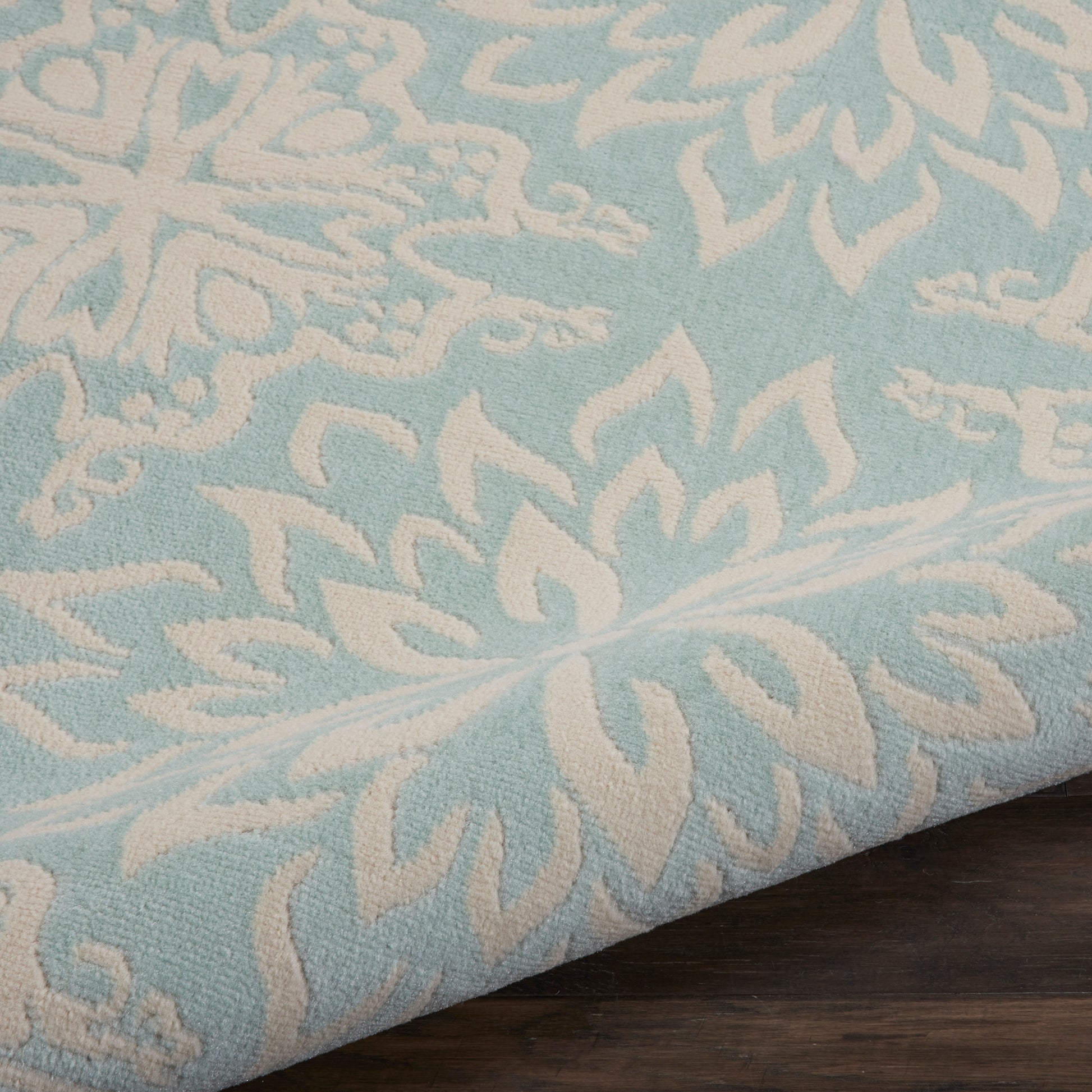 Light blue textured rug with white damask floral pattern draped over a dark wooden surface, 8' x 10'.