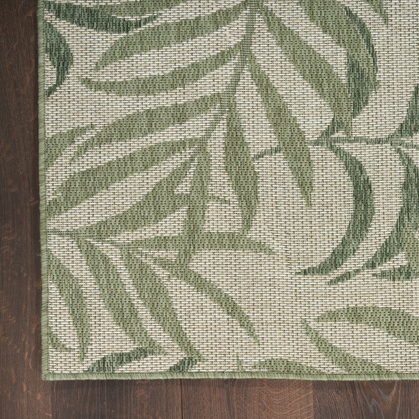 Rectangular woven rug featuring green palm leaf pattern on beige background, laid on dark wood floor.