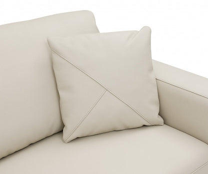 Beige faux leather sofa with a square pillow featuring an X-shaped diagonal seam.