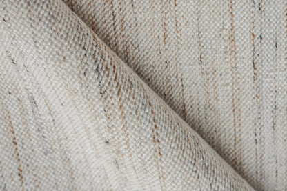 Beige flat-weave rug with cream & tan threads, diagonal fold; rustic natural textile.