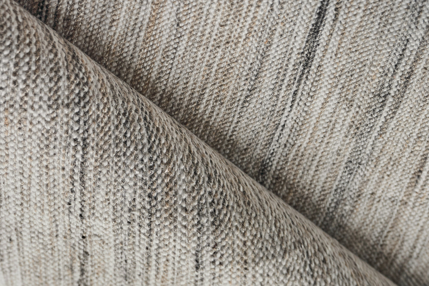 Beige & gray woven rug close-up with subtle stripes & a folded edge.