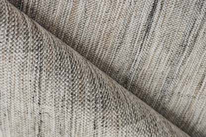 Beige & gray woven rug close-up with subtle stripes & a folded edge.