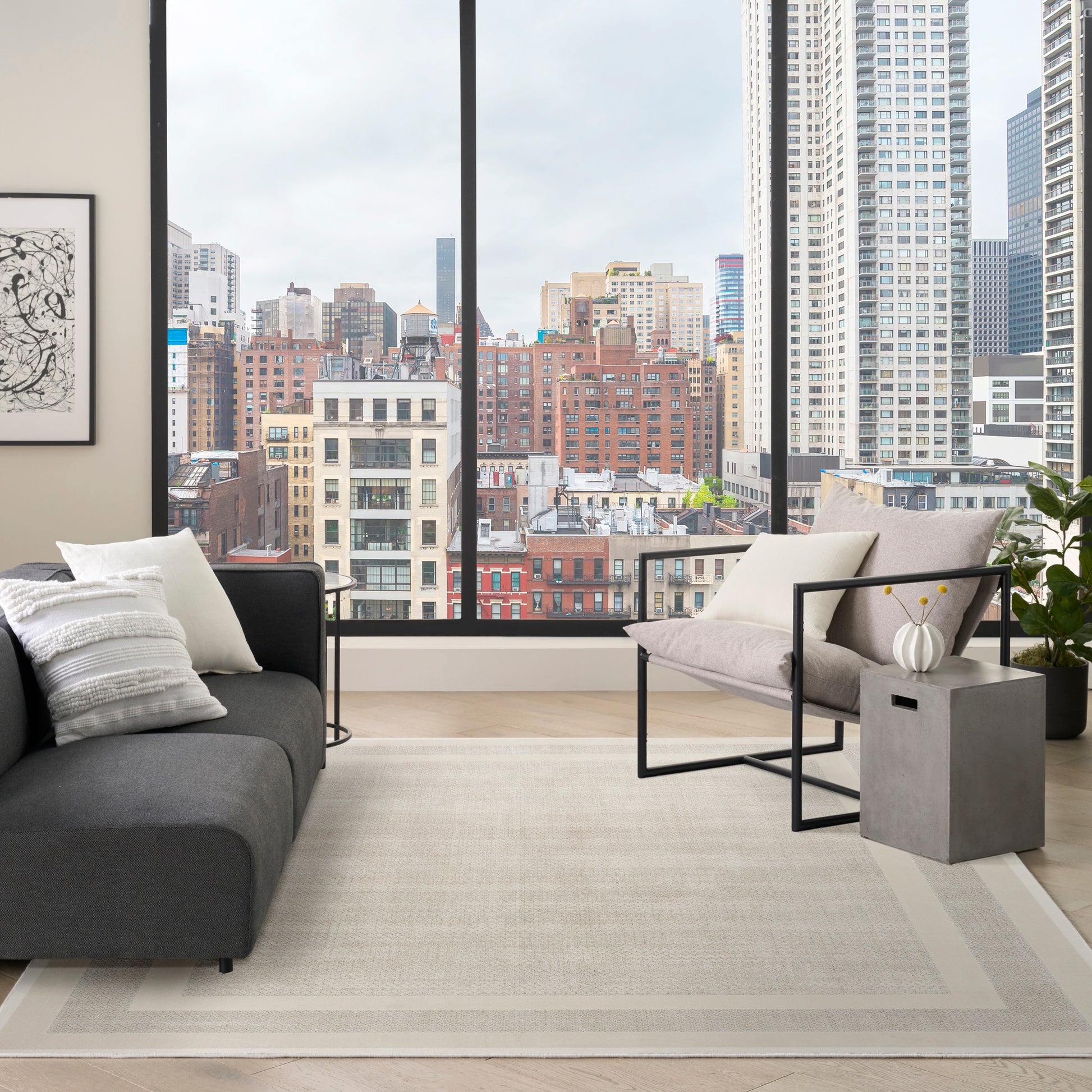 Contemporary living room with charcoal sofa, light beige rug, metal-framed chair, side table, and city skyline view.