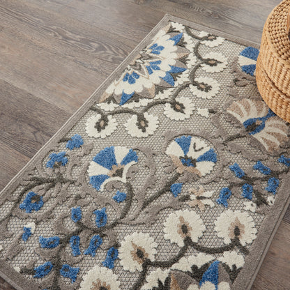 Gray floral area rug with cream and blue flowers and vine pattern, woven texture on wood floor; partial wicker basket nearby