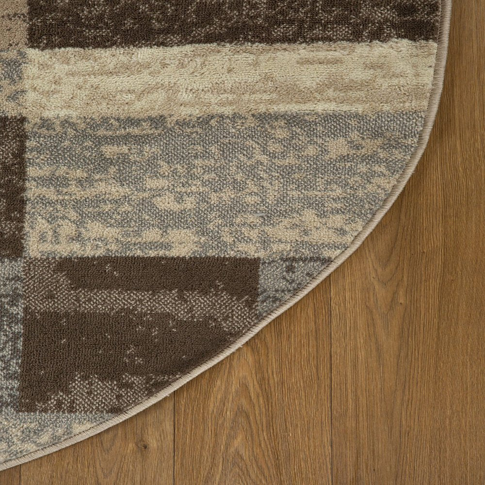 Curved edge of circular rug with brown, beige and gray geometric blocks on wood floor.