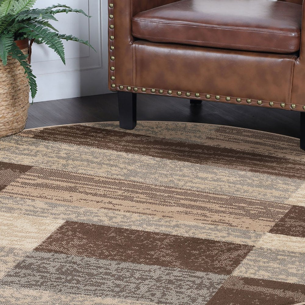 Round patchwork rug in beige, slate gray and brown with a geometric pattern, beside a plant in a woven basket.
