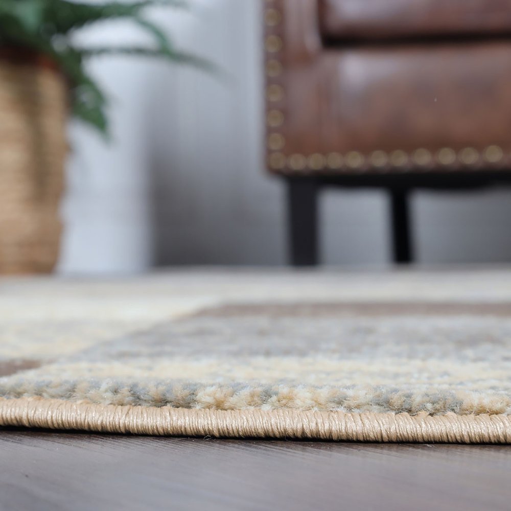 Round 8' beige slate gray and brown patchwork rug on dark wood floor; blurred brown leather chair in living room.