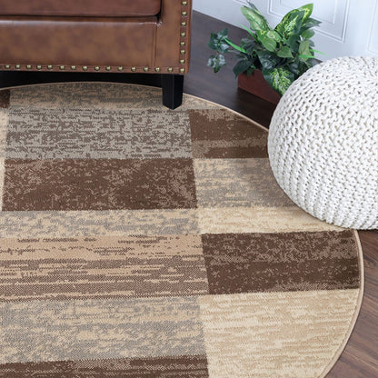 8' round patchwork rug in beige, slate gray and brown under a studded leather chair, with a white knitted pouf and a green plant nearby.