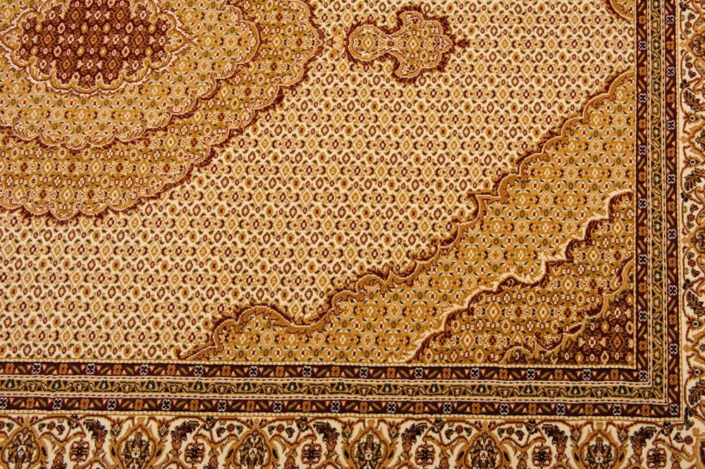 Persian-style rug close-up with warm beige, gold & brown tones, intricate medallion and floral border.