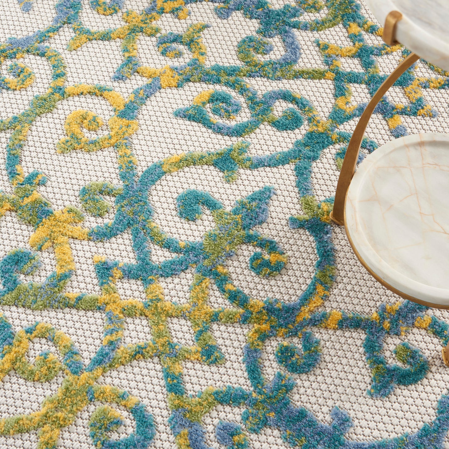 Beige woven rug with turquoise and mustard scrolling pattern; partial round marble tray with tan leather strap.