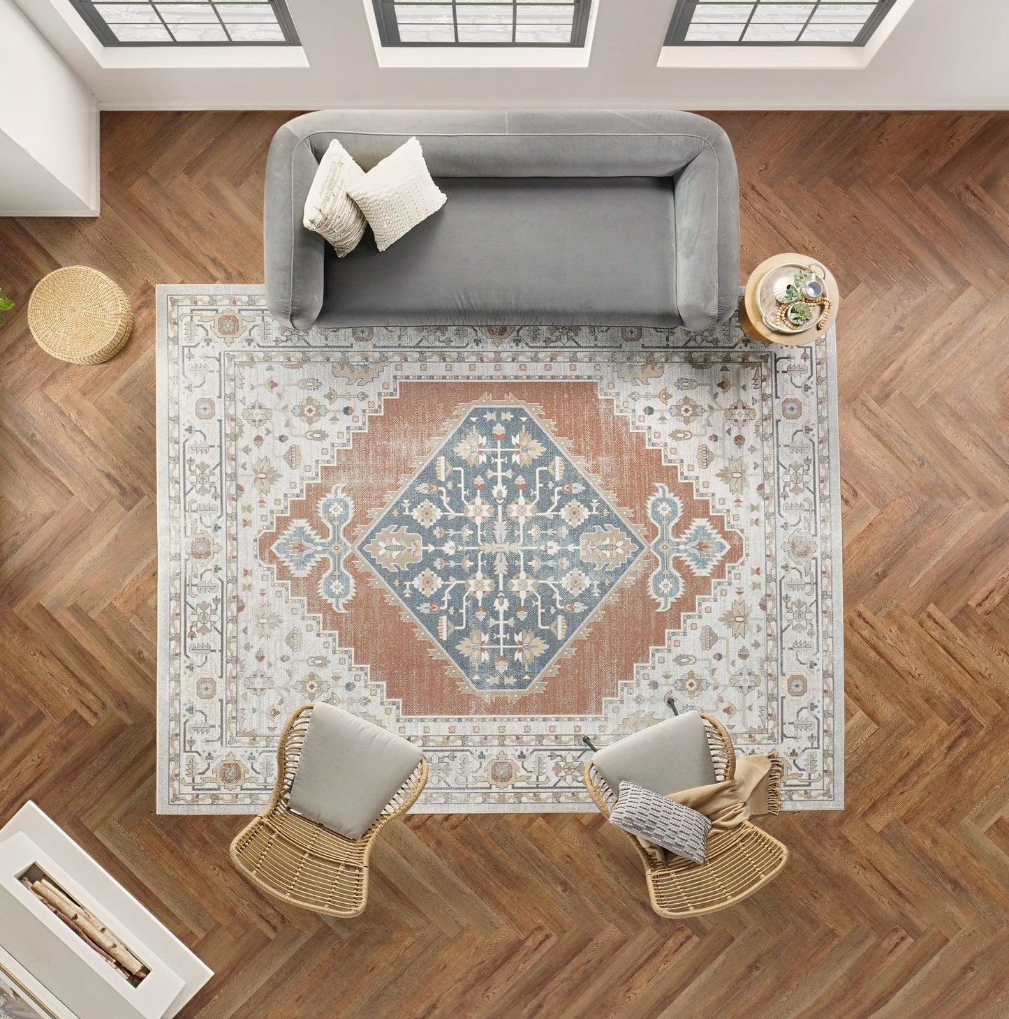 Top-down living room with blue-rust-ivory oriental rug, gray sofa, two wicker chairs, and a round side table with a plant.
