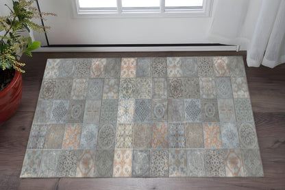 Rectangular patchwork rug in muted blues, grays and beiges with geometric patterns on a dark wood floor beside a plant.