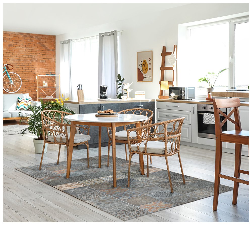 Bright open-plan kitchen and dining area with round white table, rattan chairs, brick accent wall, turquoise bike decor, and potted plants.