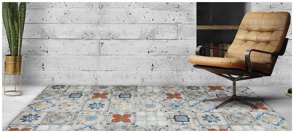 Industrial living room with tufted tan leather lounge chair, blue-and-orange patterned tile floor, concrete wall, and tall green plant.