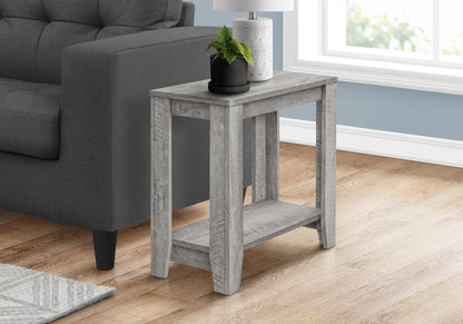 Weathered gray wood end table with lower shelf beside a gray sofa; top with black plant pot and white ceramic lamp.