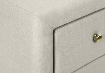 Beige linen-textured upholstered drawer unit with round brass knob & clean, modern rectangular design.
