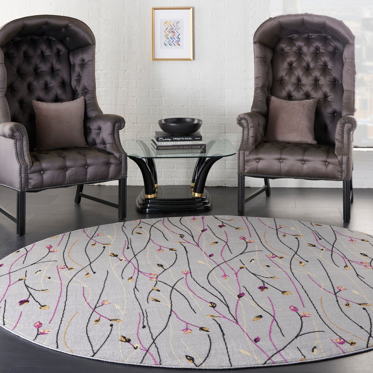 Round area rug with purple, pink, gold vine patterns beneath tufted dark brown leather club chairs and a glass coffee table.