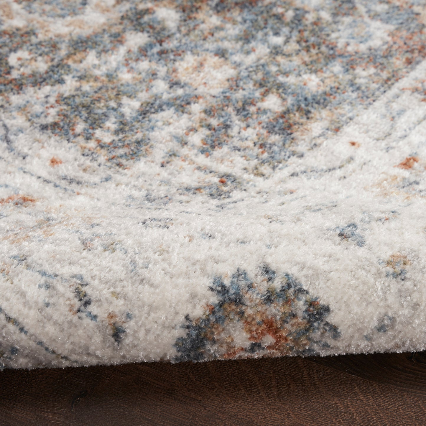 Close-up of a plush runner rug with ivory cream base, blue-gray and rust accents, soft textured pile and folded edge.
