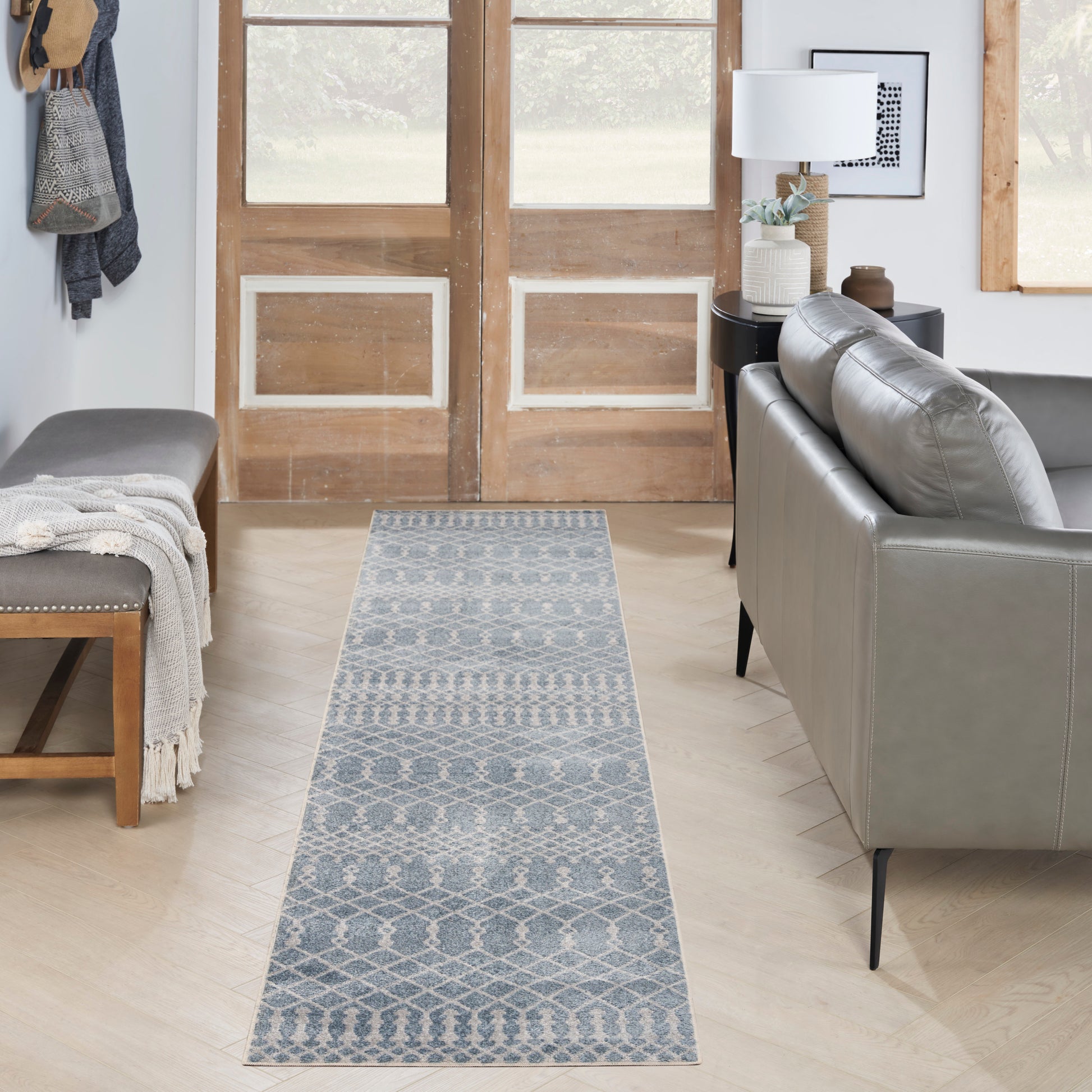 Blue-gray geometric runner rug in a cozy living room hallway with wooden doors, a gray sofa, and bench.