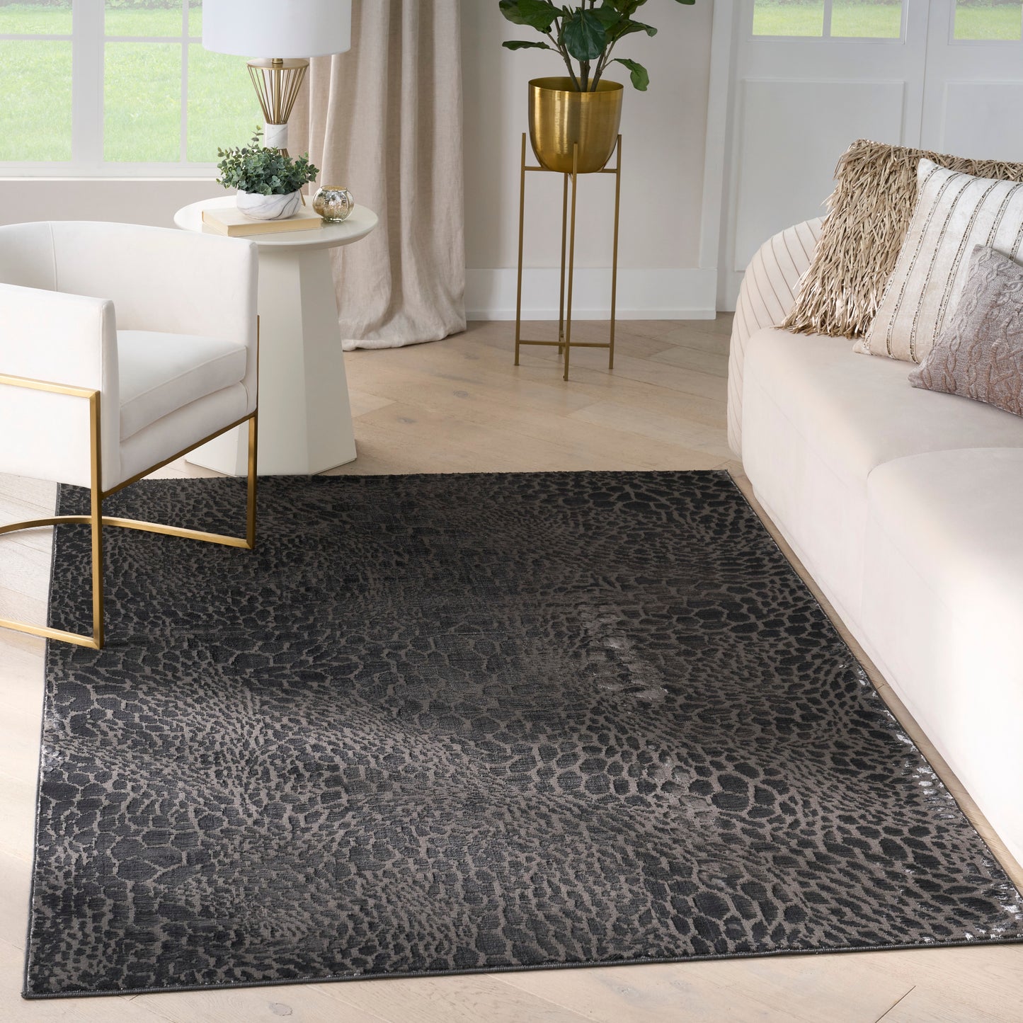 Rectangular leopard-print area rug in black & charcoal on light wood floor, with white sofa & chair with gold metal frames.