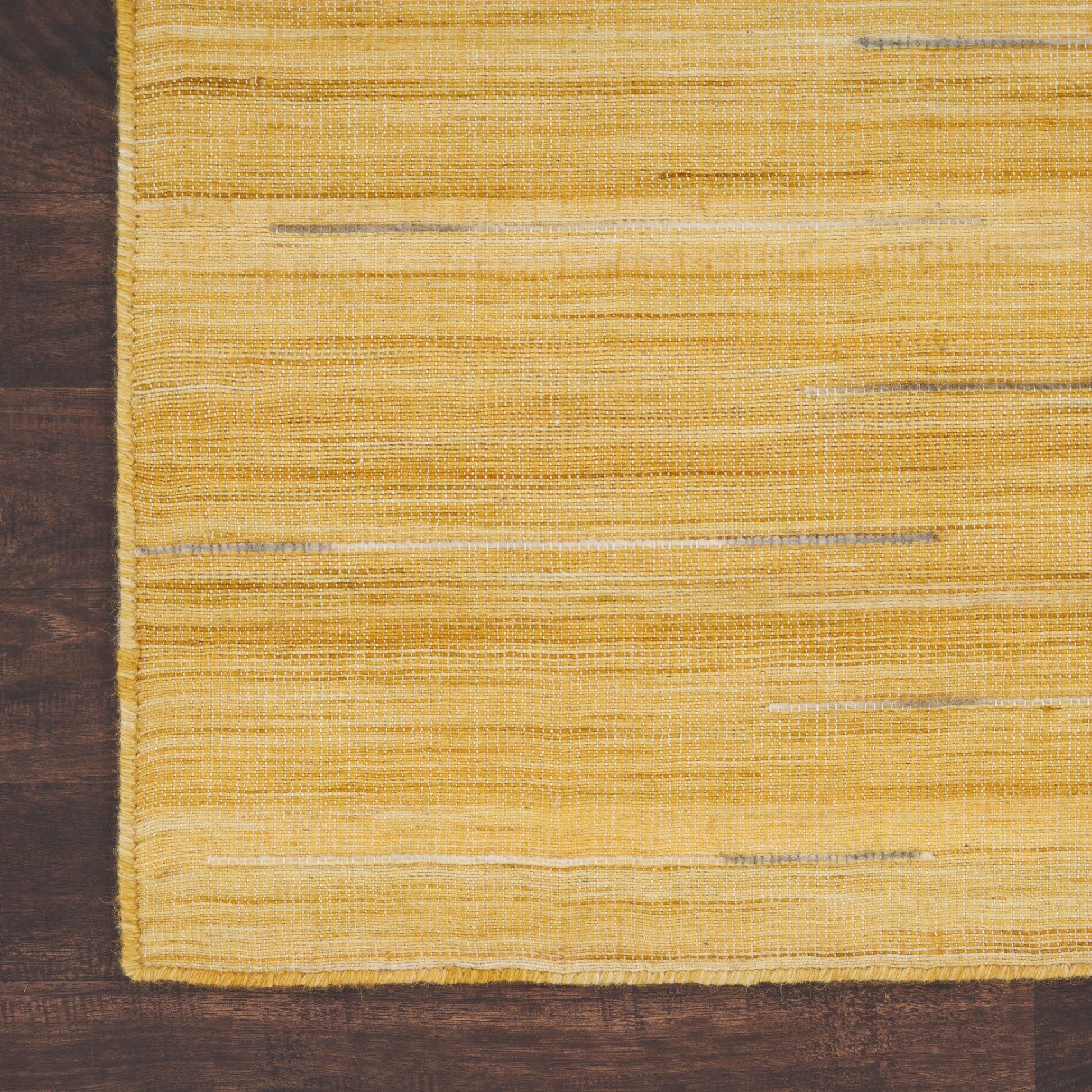Rectangular bright yellow flatwoven rug with subtle horizontal stripes on dark wood floor.