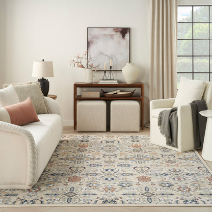 Cream upholstered sofa and armchair, beige pillows, wooden console, two beige ottomans, blue-beige patterned rug.