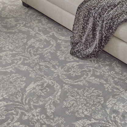 Gray damask-patterned area rug beneath a light beige sofa with a chunky gray knit throw.