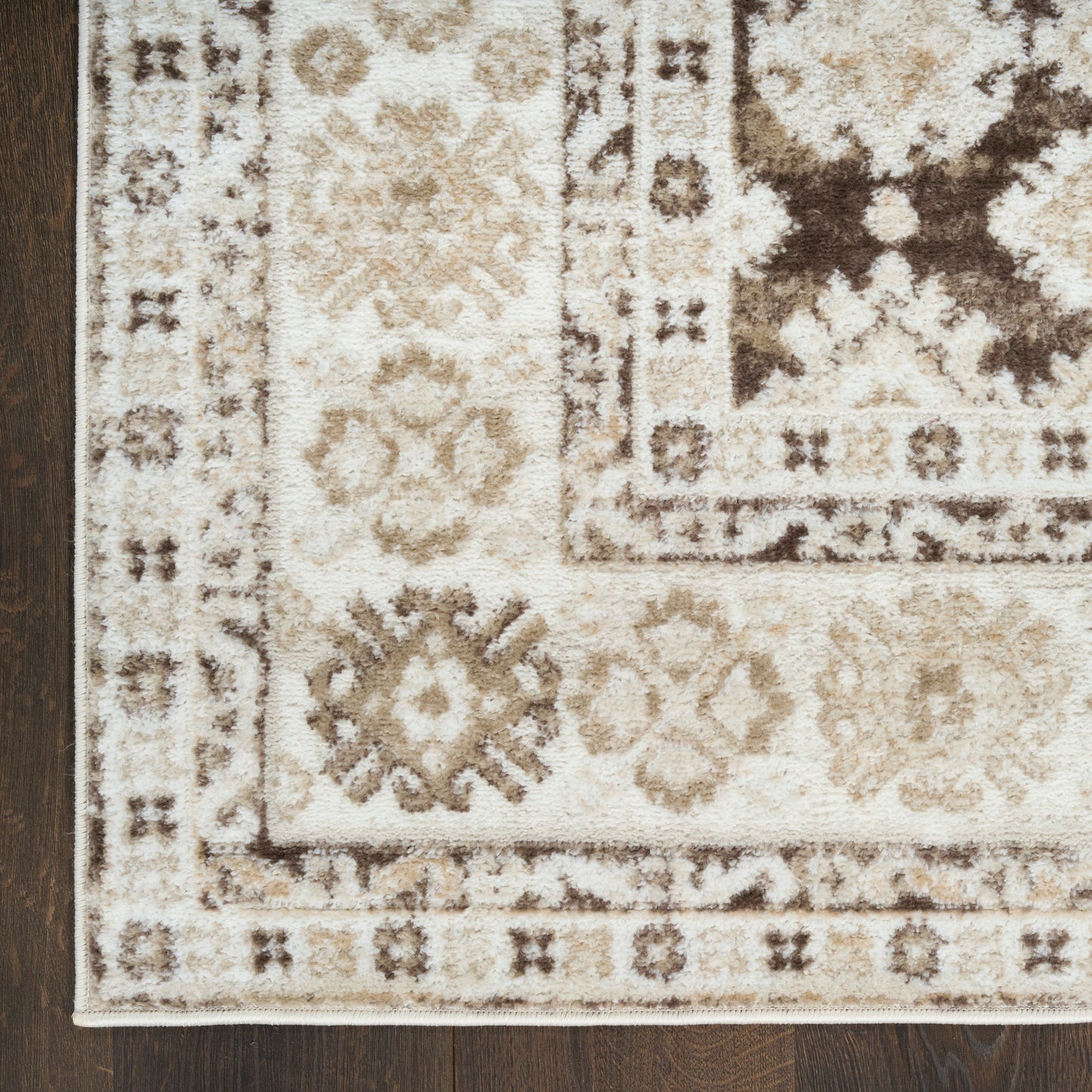 Beige oriental rug with brown floral medallions and geometric border on dark wood floor.