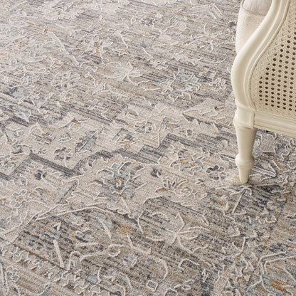 Neutral-toned area rug with faded floral pattern in gray, beige and ivory; cream carved chair leg visible on the right.