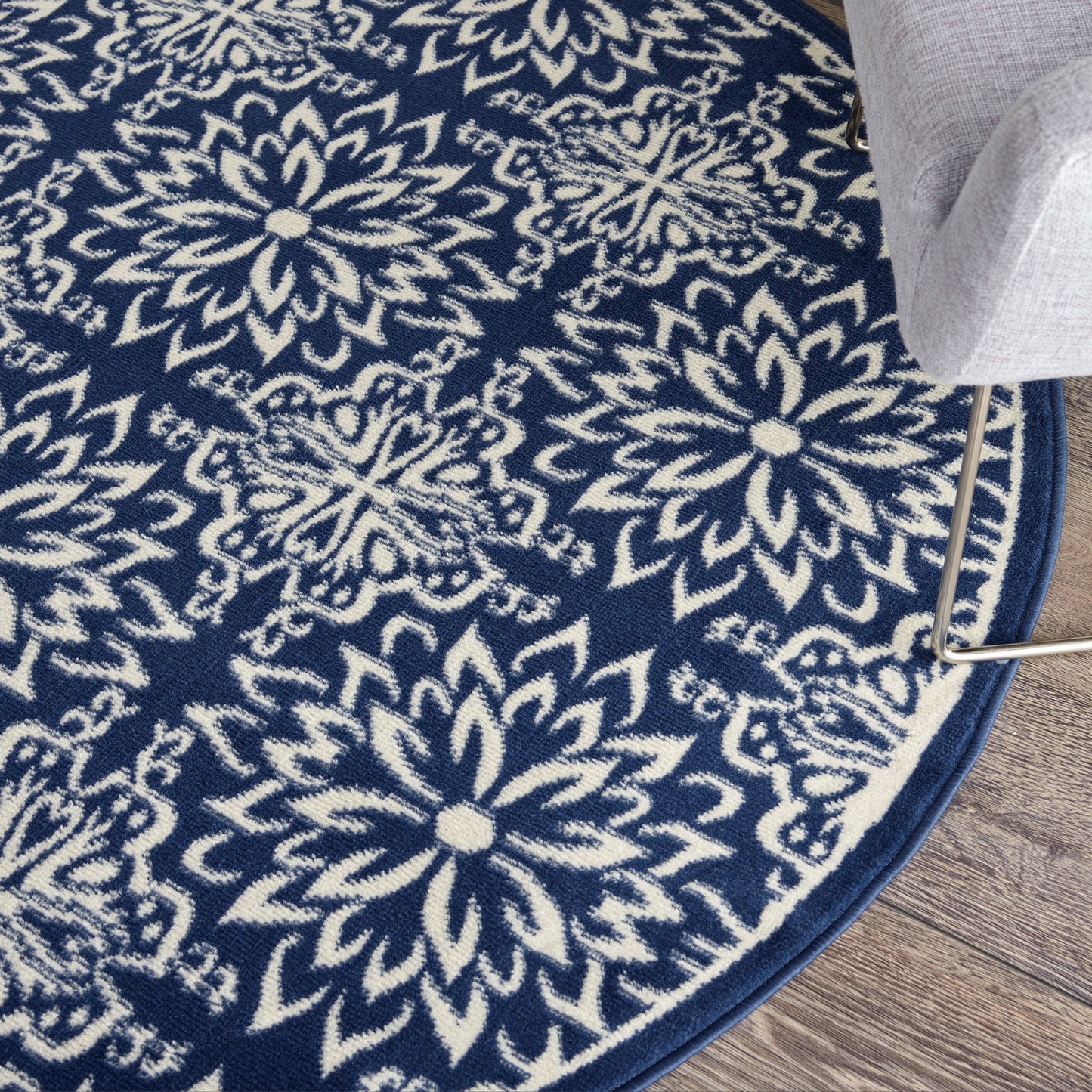 Round navy blue rug with white floral mandala pattern on wood floor, border edge visible beside a gray sofa leg.