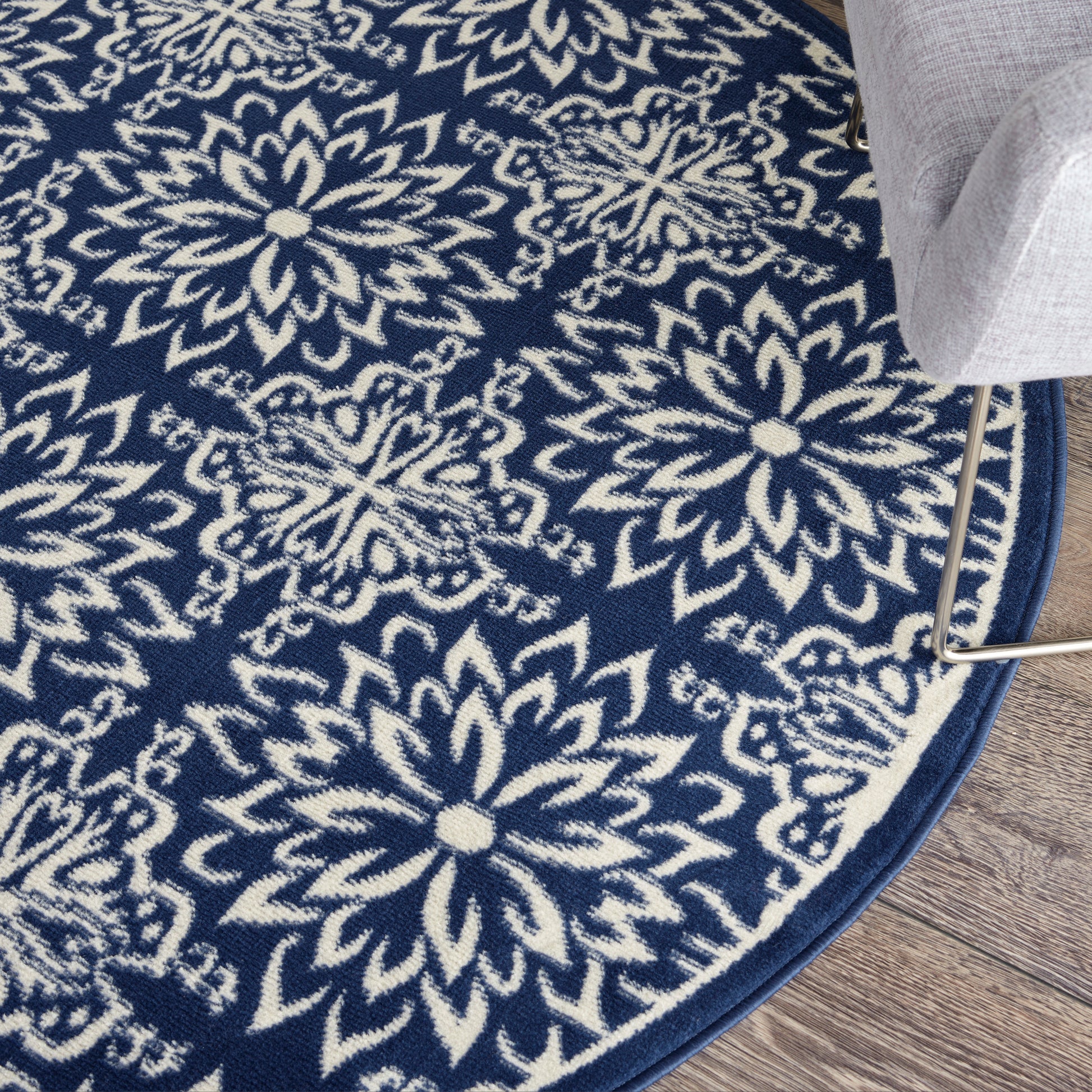 Round navy blue rug with white floral mandala pattern on wood floor, border edge visible beside a gray sofa leg.