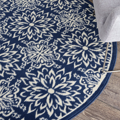 Round navy blue rug with white floral mandala pattern on wood floor, border edge visible beside a gray sofa leg.