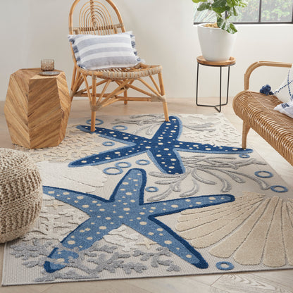 Coastal living room with a blue starfish-pattern area rug, wicker rattan chairs, striped pillows, wooden side table, and a potted plant.