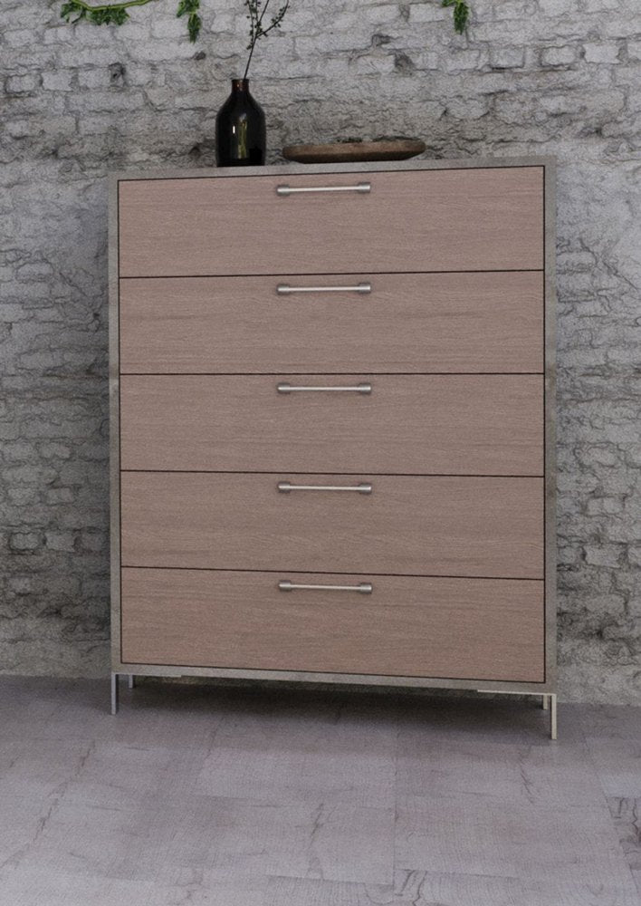 Light wood five-drawer chest with silver handles on slim metal legs, brick wall backdrop, decorative vase on top.