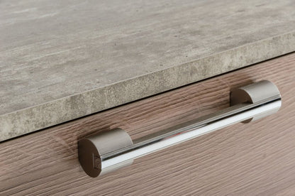 Modern chrome cylindrical pull handle on a light wood cabinet drawer beneath a gray stone countertop.