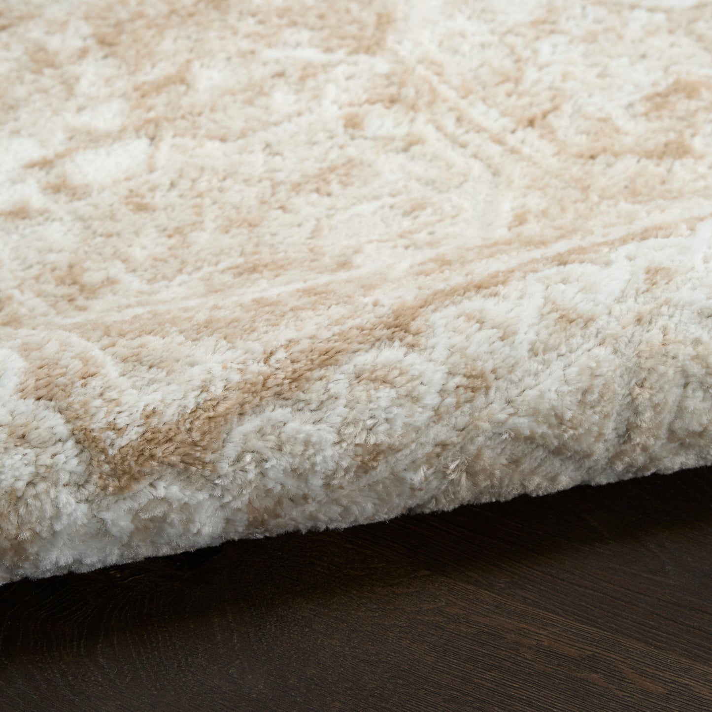 Close-up of a soft beige cream shag rug edge on dark wood flooring.
