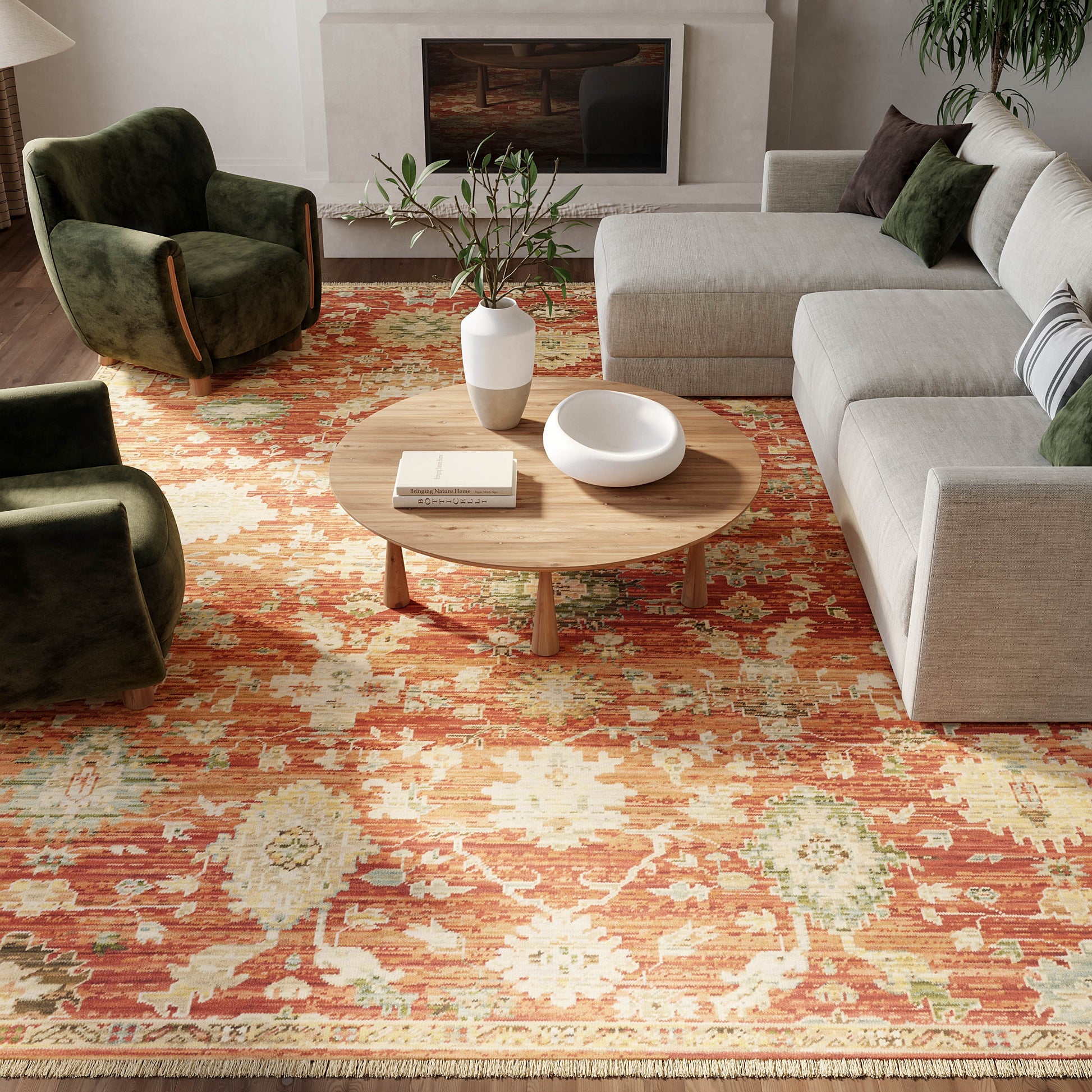 Cozy living room with round wooden coffee table on a vivid orange floral rug, gray sectional sofa and green velvet armchairs.