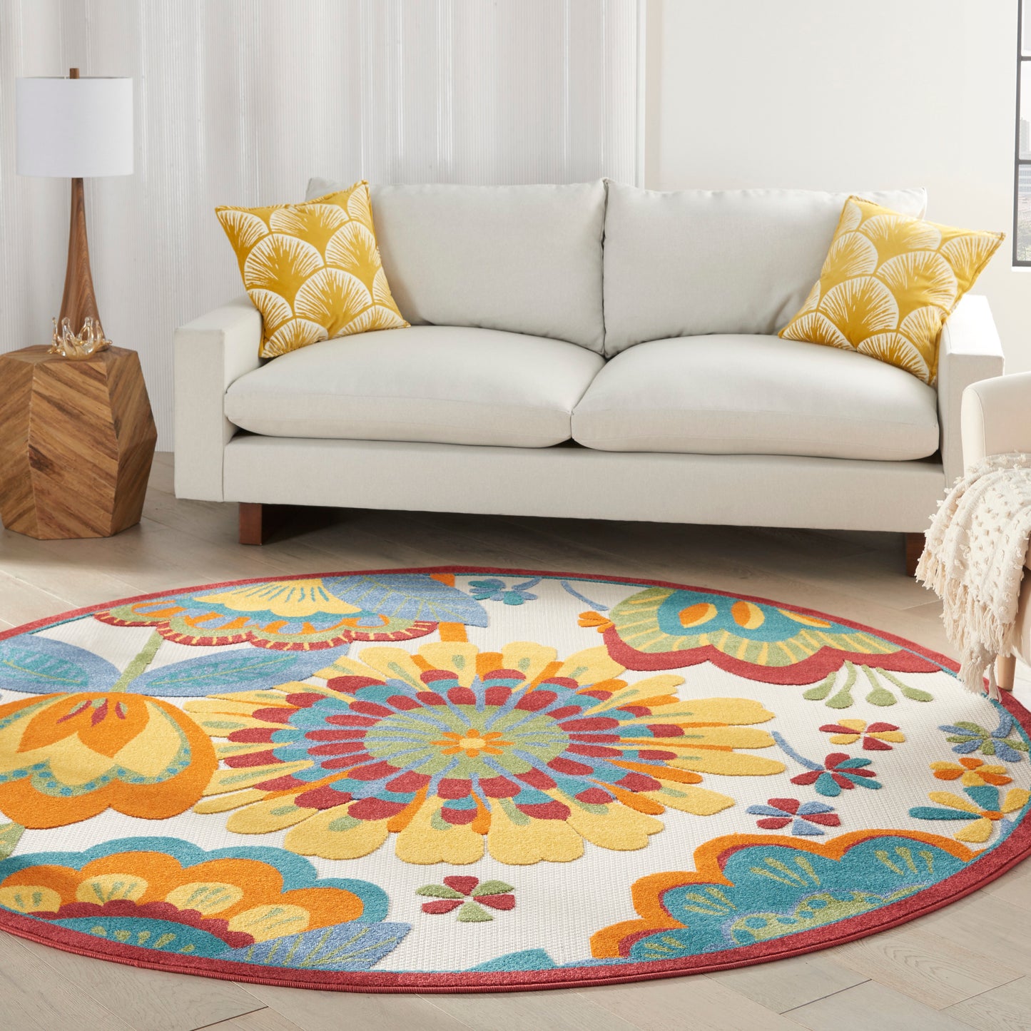 Living room with a light gray sofa, yellow patterned pillows, a wooden geometric side table, and a round colorful floral rug.