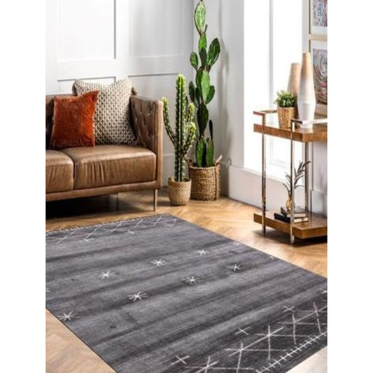 Gray hand loomed area rug with subtle white star motifs in a modern living room & tan leather sofa, potted plants & wooden furniture.