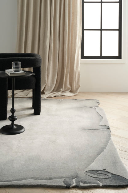 Black curved chair with a small round side table and glass, atop a light gray rug; beige curtains and grid window.