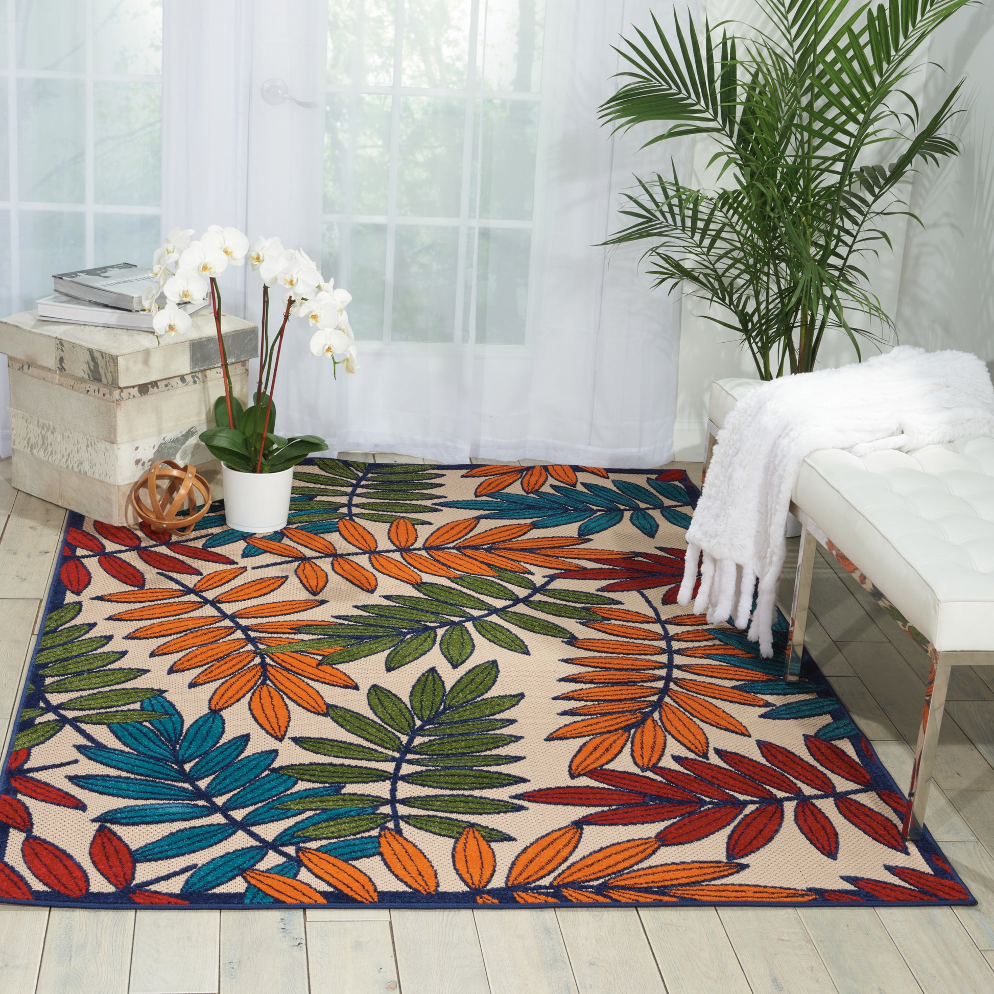 Colorful tropical leaf-pattern area rug in orange, teal, blue, green; bright living room with white furniture and plants.