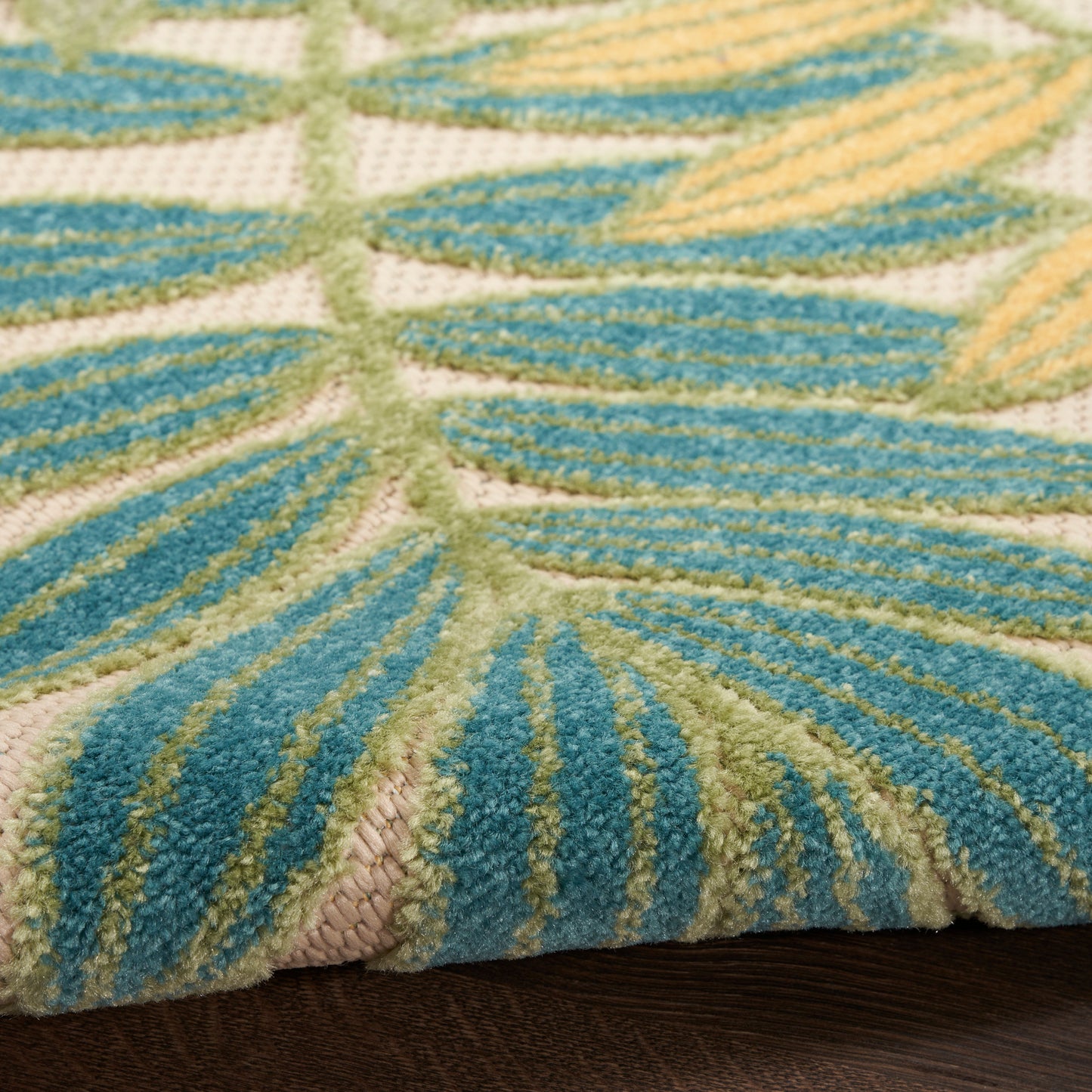 Close-up of a plush teal & lime leaf-pattern rug with beige background on dark wood floor.