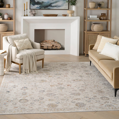 Cozy neutral living room with beige sofa and armchair, light wood shelves, patterned rug, and fireplace with art above.