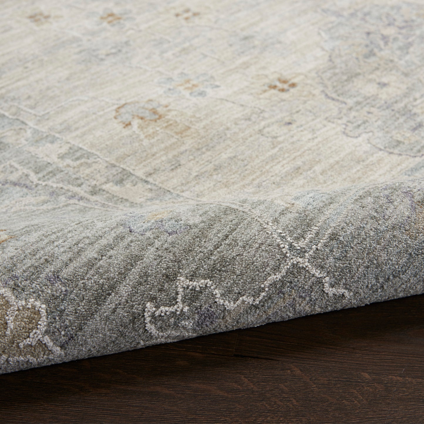 Light beige and gray distressed area rug with subtle floral and geometric border, low-pile on dark wood floor.