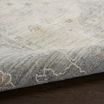Light beige and gray distressed area rug with subtle floral and geometric border, low-pile on dark wood floor.