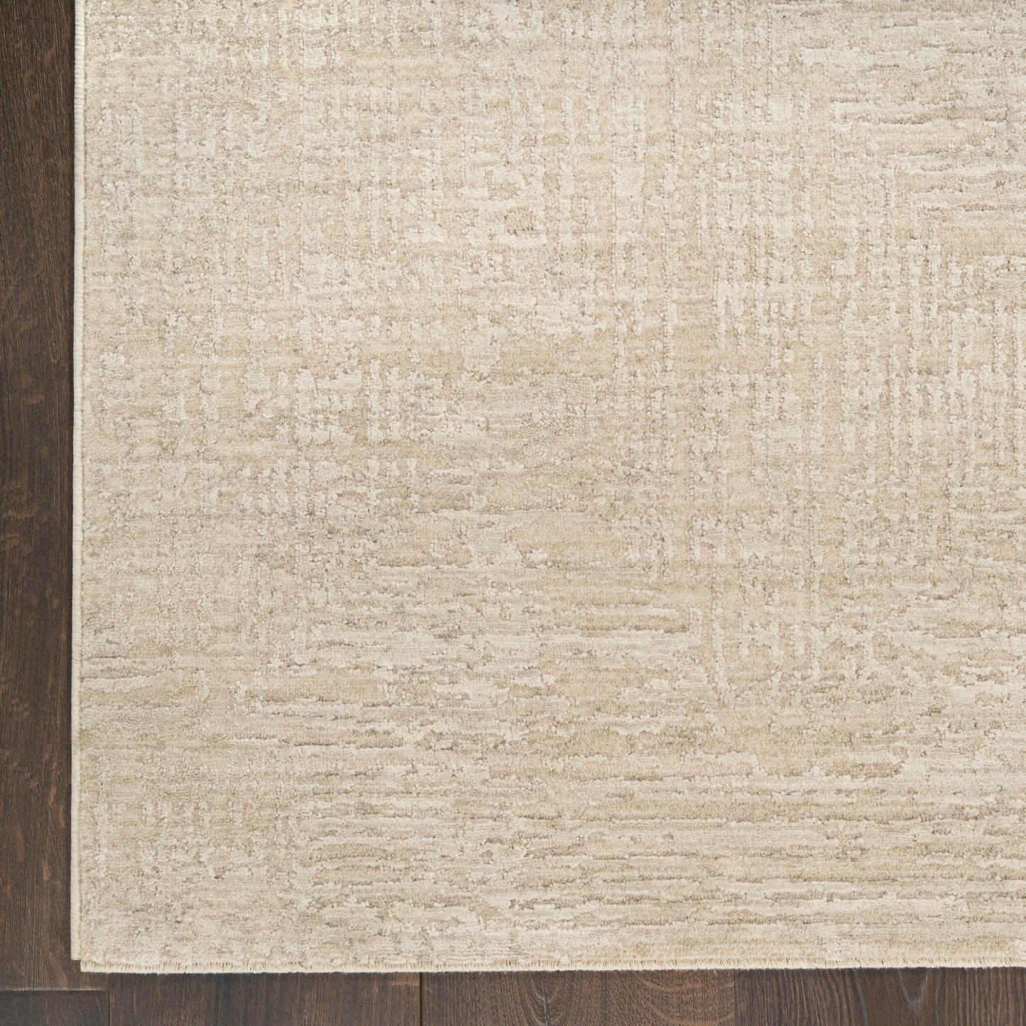 Beige rectangular textured area rug with a subtle pattern laid over dark wood flooring.