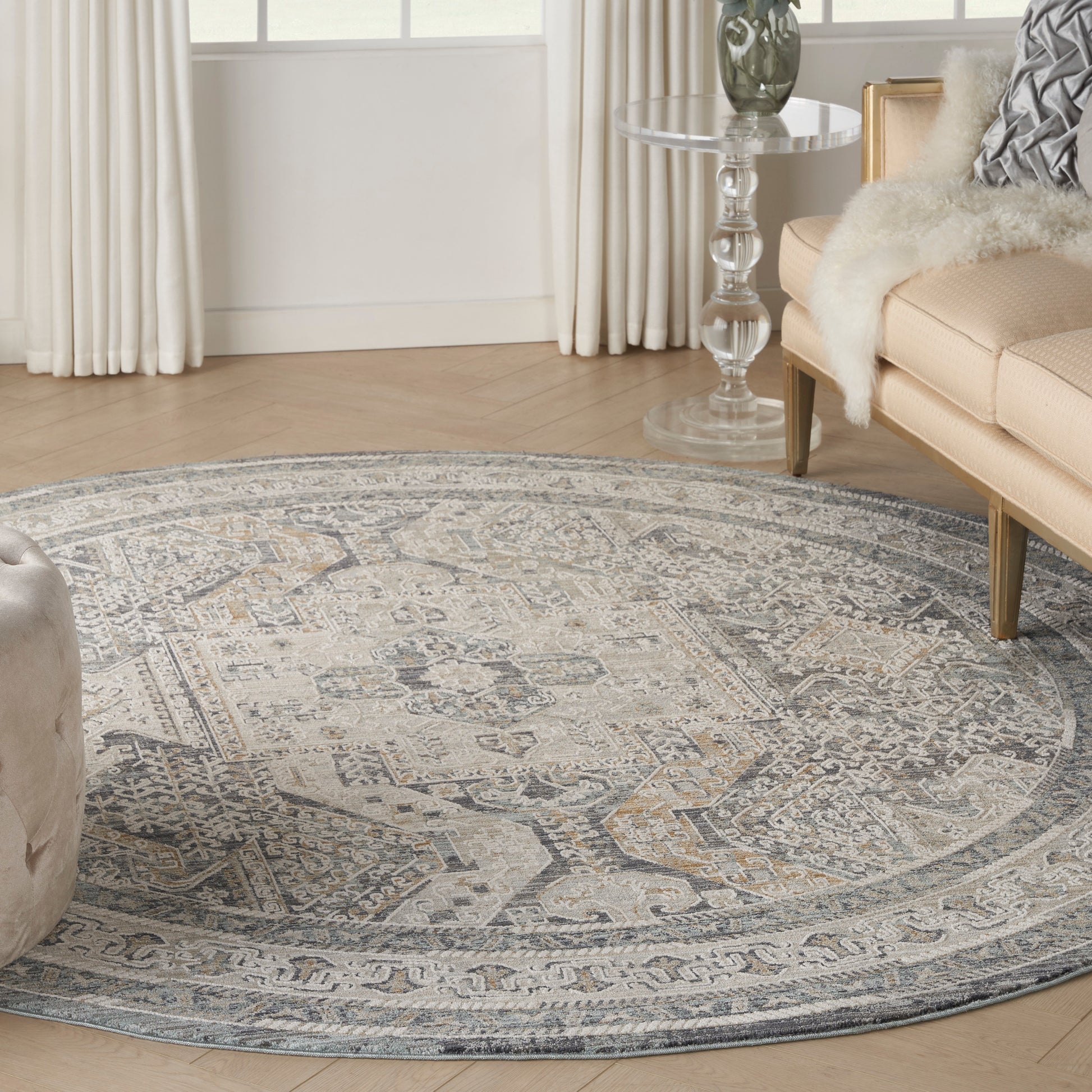 Round area rug with intricate gray-blue medallion pattern on light wood floor in a cozy living room.