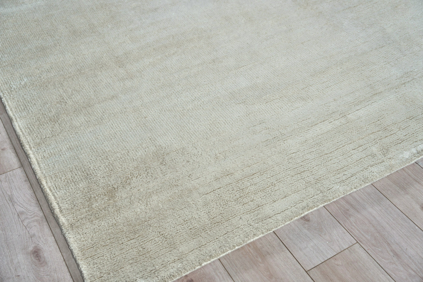 Beige-gray hand-knotted area rug on light wood floor, subtle texture, modern minimalist style.