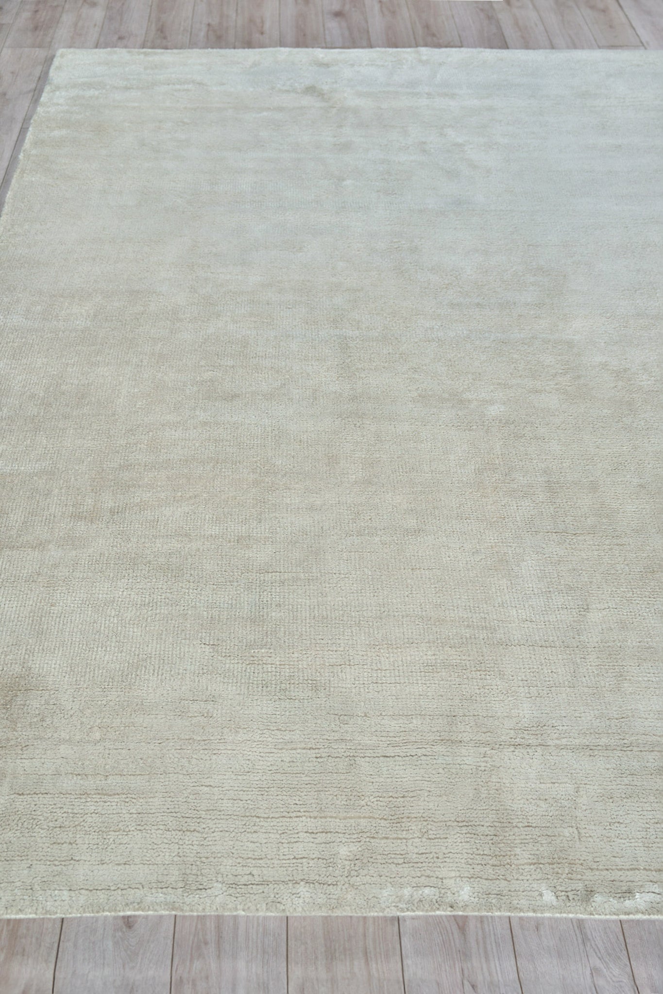Rectangular cream-beige plush indoor hand-knotted rug with subtle texture on a light wooden floor.