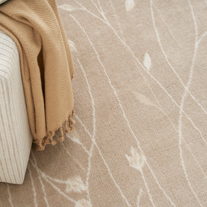 Beige rug with white branch-like pattern, draped tan woven blanket with tassels over a light striped sofa.
